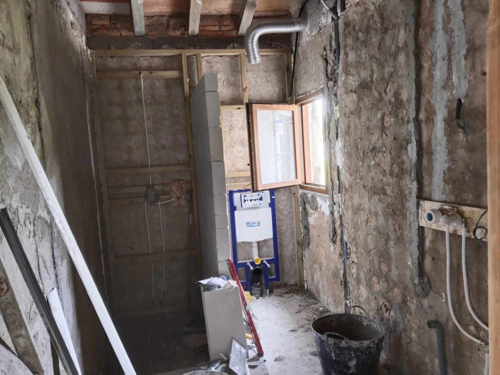 Baño en obra con paredes picadas, bastidor del inodoro empotrado y tuberías vistas
