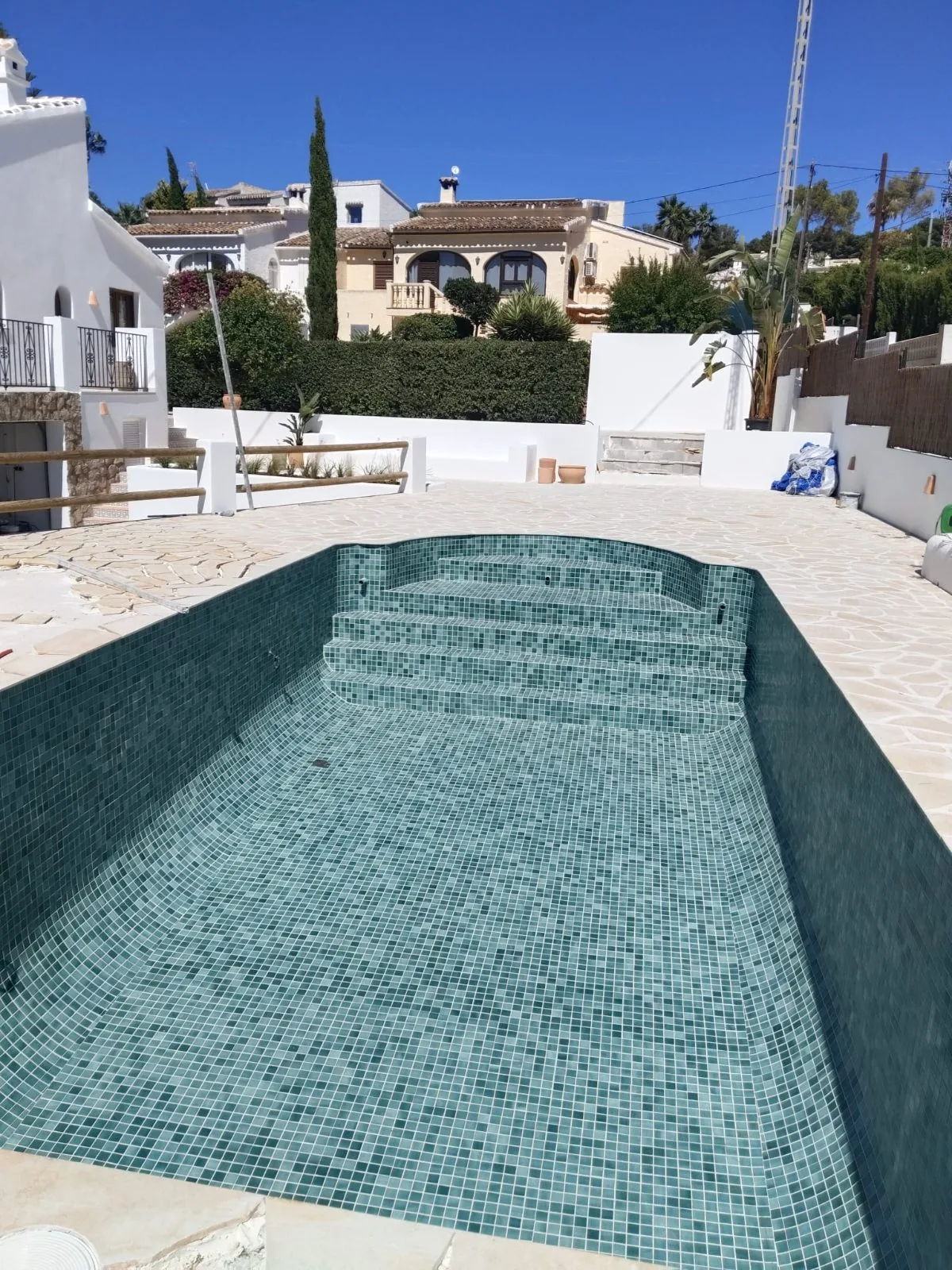 Piscina alargada con mosaico verde y escalera de acceso, rodeada de terraza de piedra